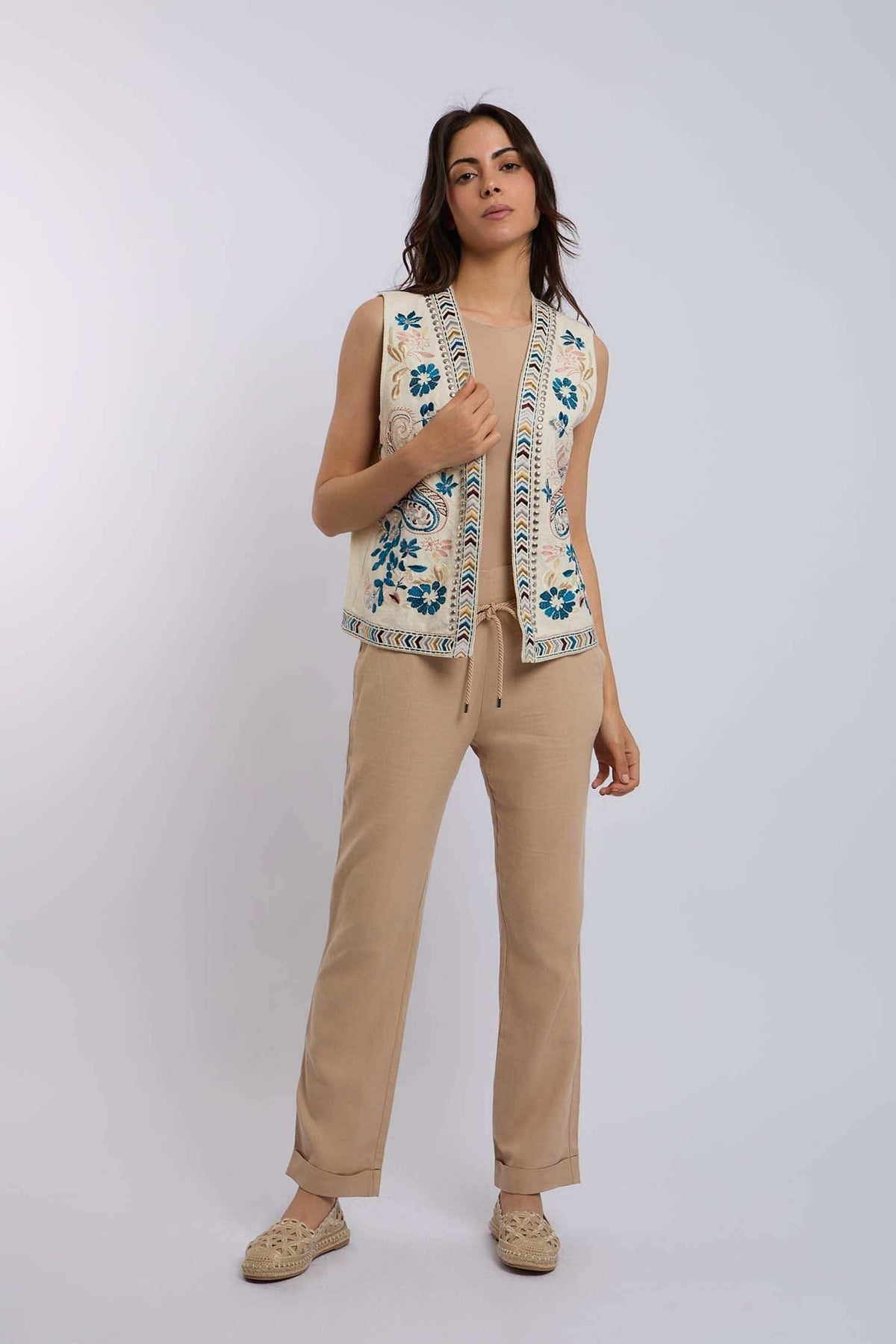 Woman wearing sleeveless embroidered vest with floral pattern over beige casual outfit
