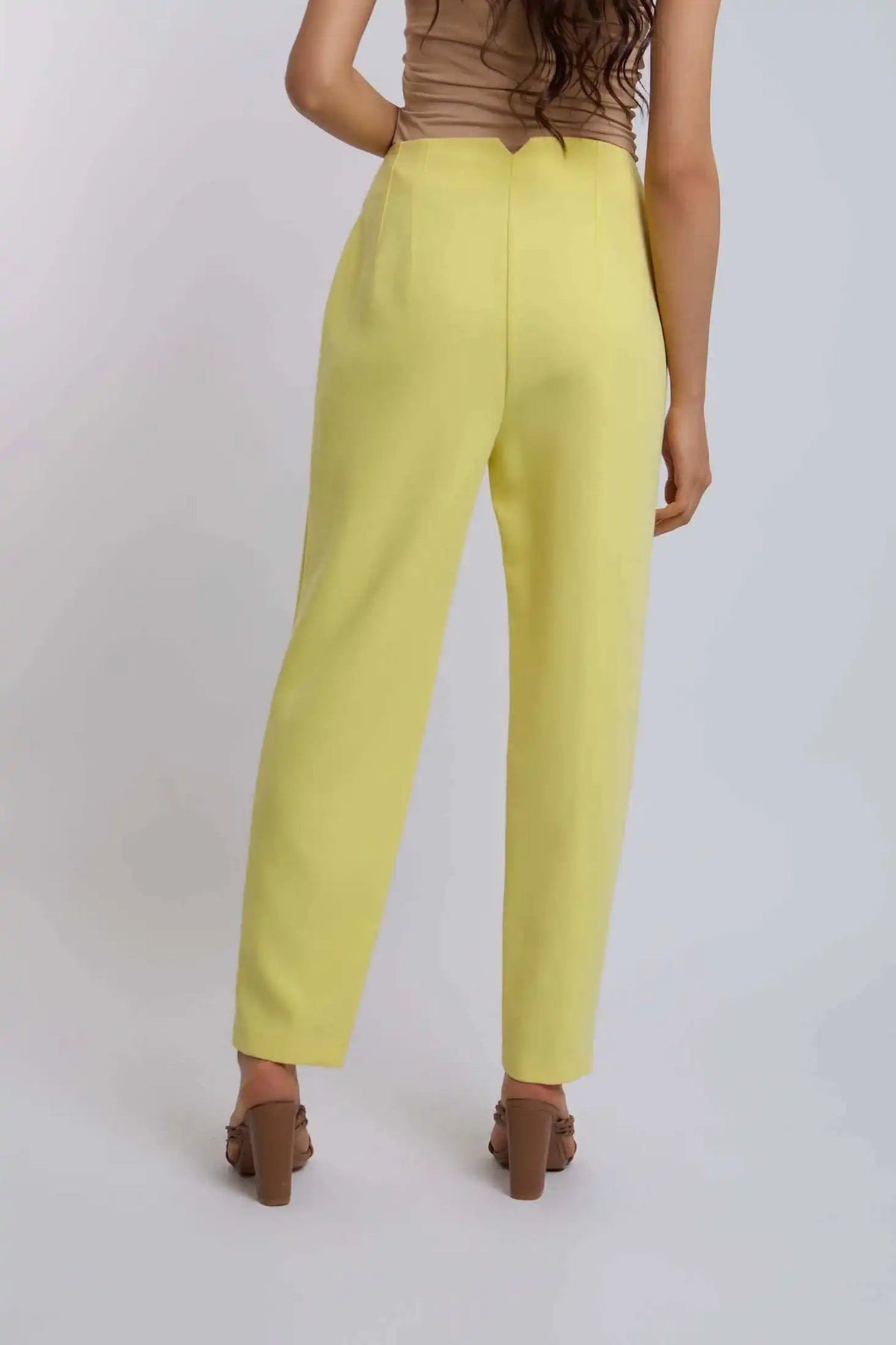 Woman wearing high-waisted yellow pants and brown heels, back view, casual fashion