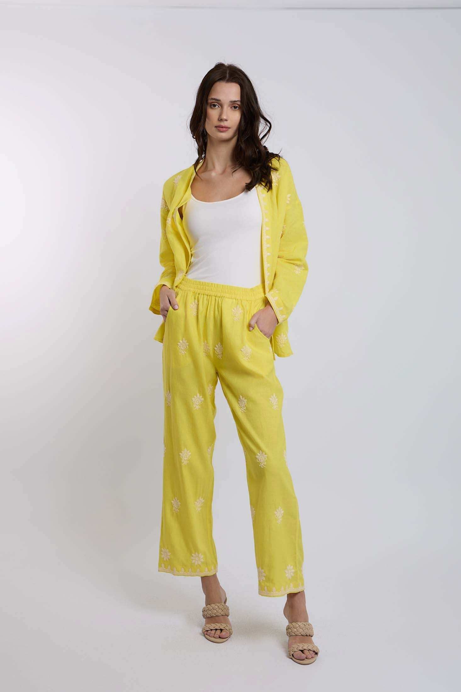 Woman wearing a yellow embroidered pants and jacket set with white tank top, standing in studio