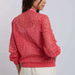 Woman wearing a coral eyelet lace blouse with long sleeves and cream pants, back view
