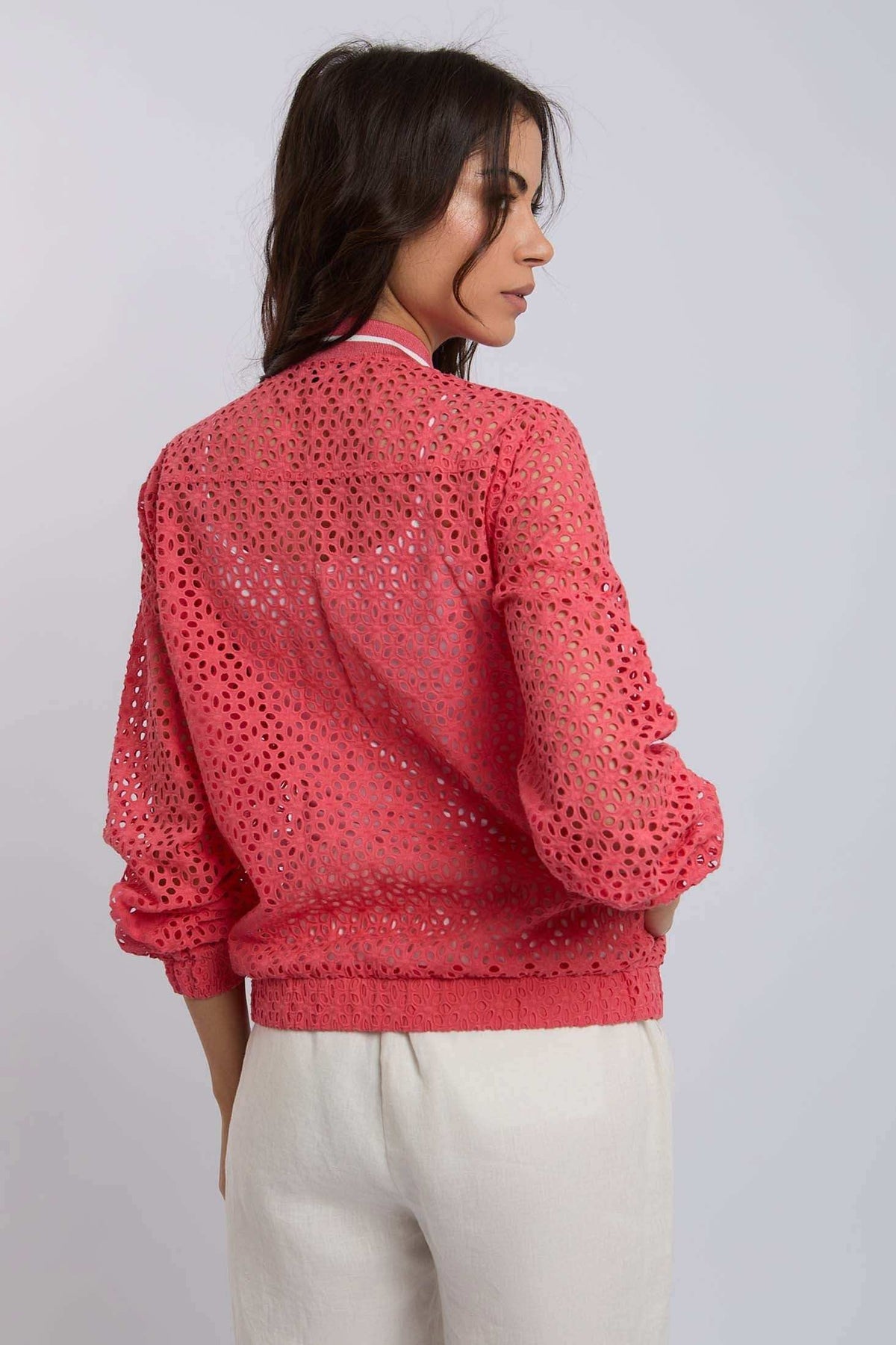 Woman wearing a coral eyelet lace blouse with long sleeves and cream pants, back view