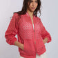 Woman wearing a coral pink eyelet bomber jacket with zipper and white pants