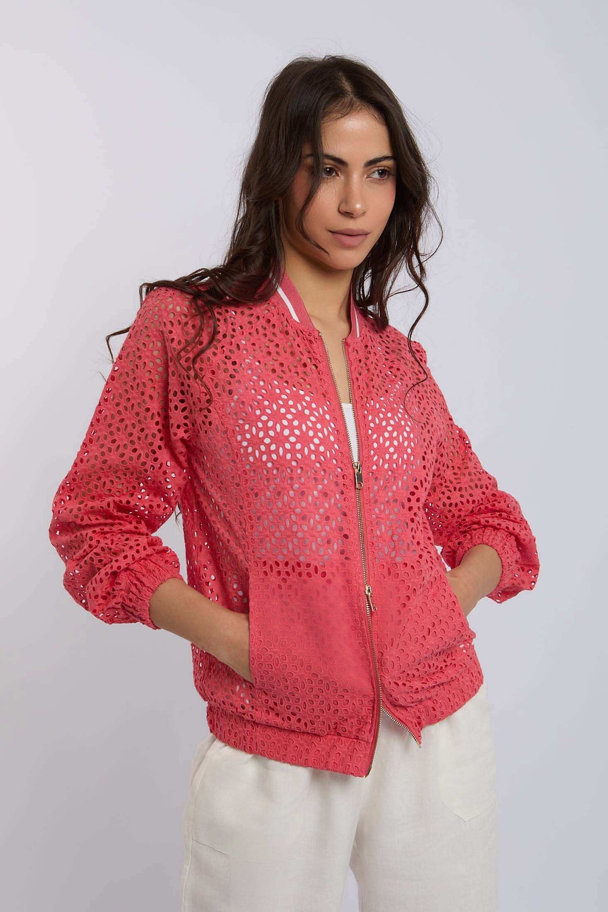 Woman wearing a coral pink eyelet bomber jacket with zipper and white pants
