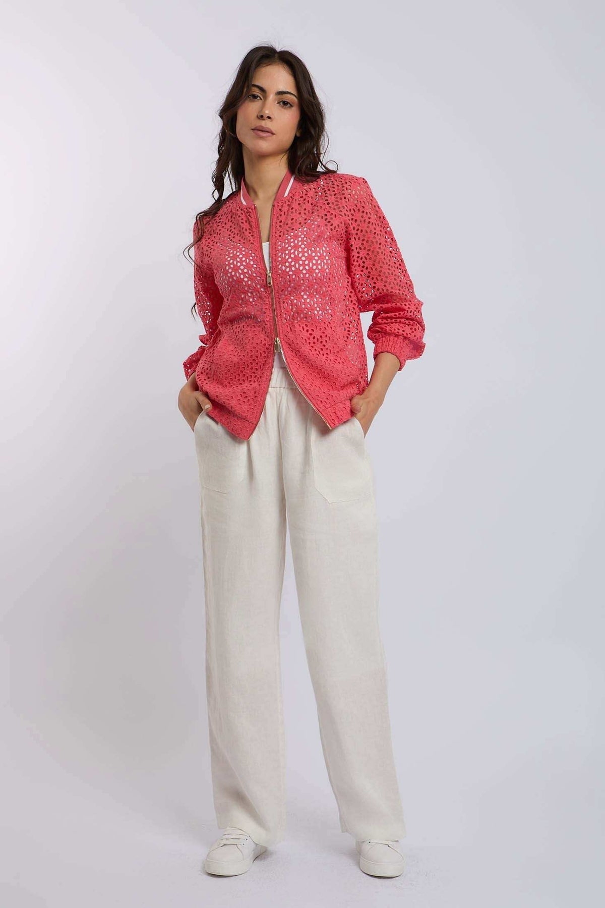 Woman wearing a pink eyelet bomber jacket with white wide-leg pants and white sneakers