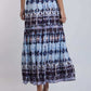 Woman wearing a blue and black patterned maxi skirt with white top and heeled sandals