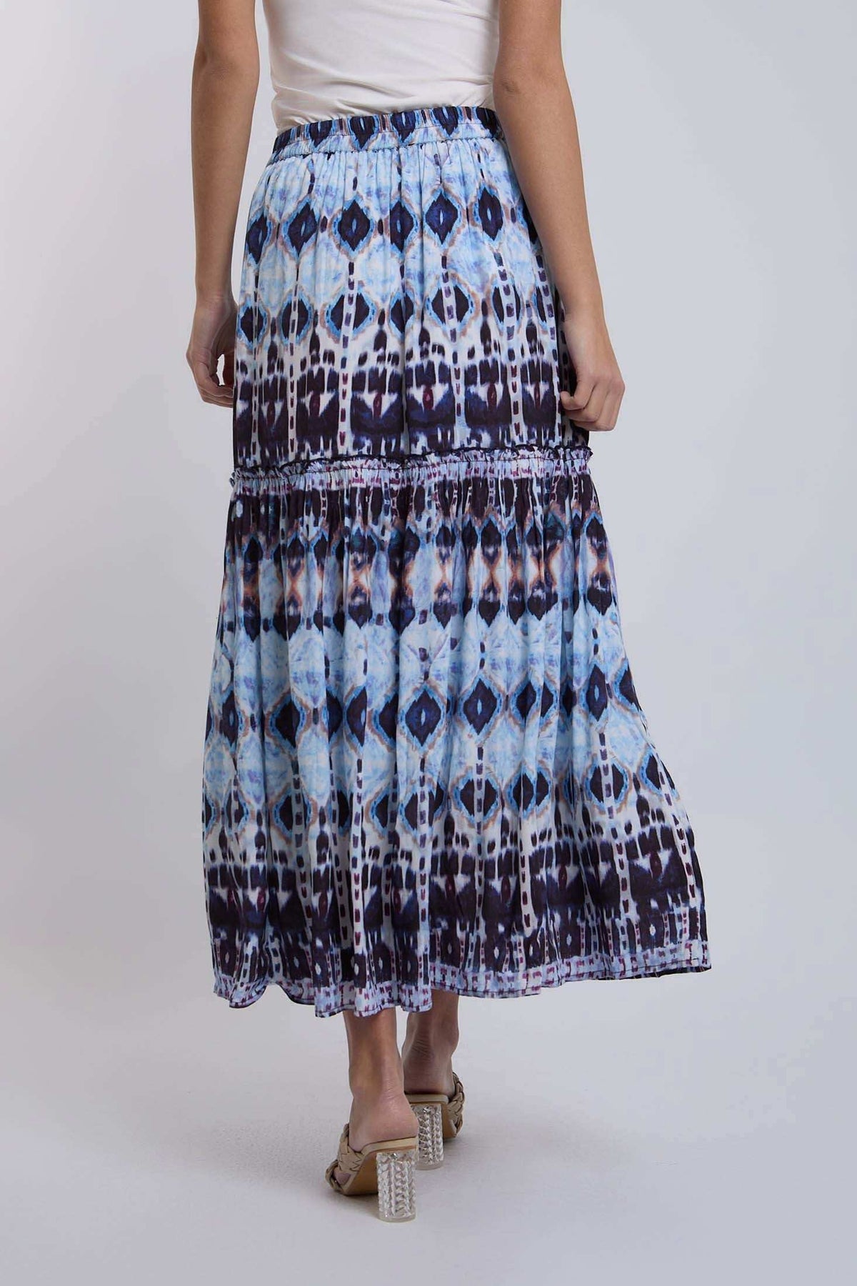 Woman wearing a blue and black patterned maxi skirt with white top and heeled sandals