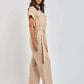 Woman in a beige linen jumpsuit with waist tie and wide legs, styled with heeled sandals