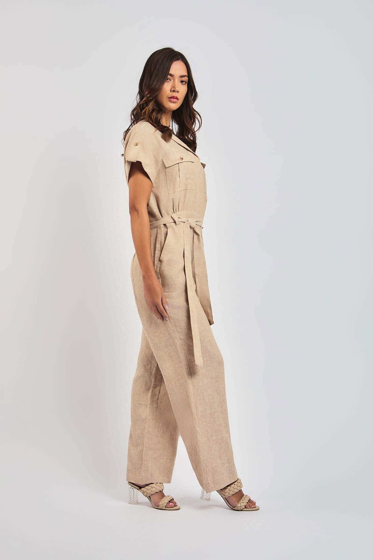 Woman in a beige linen jumpsuit with waist tie and wide legs, styled with heeled sandals