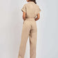 Woman wearing beige short sleeve belted linen jumpsuit, standing with back view