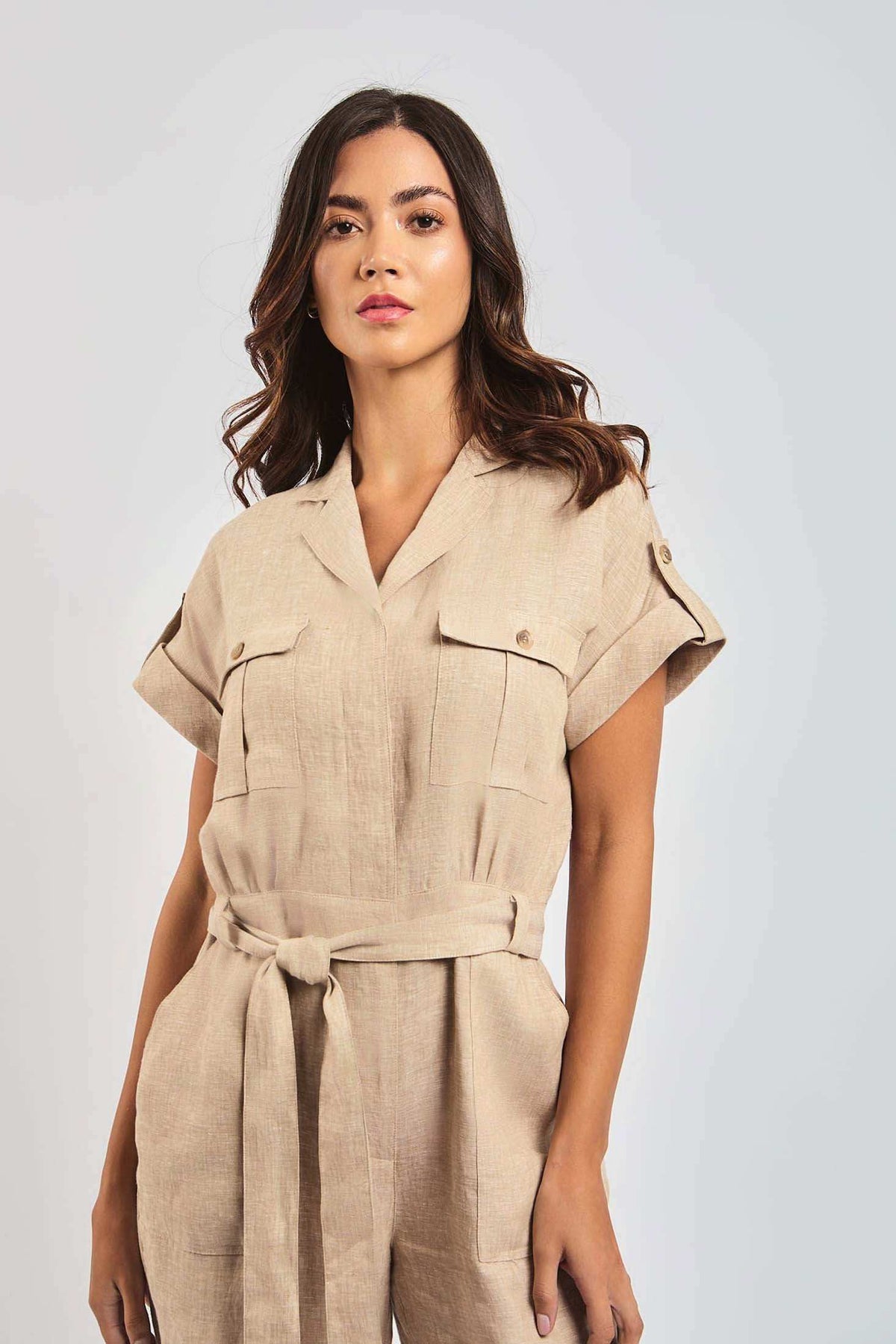Woman wearing beige linen short-sleeve belted jumpsuit with front pockets