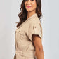 Woman wearing short sleeve beige belted jumpsuit with side pockets, posing on light background