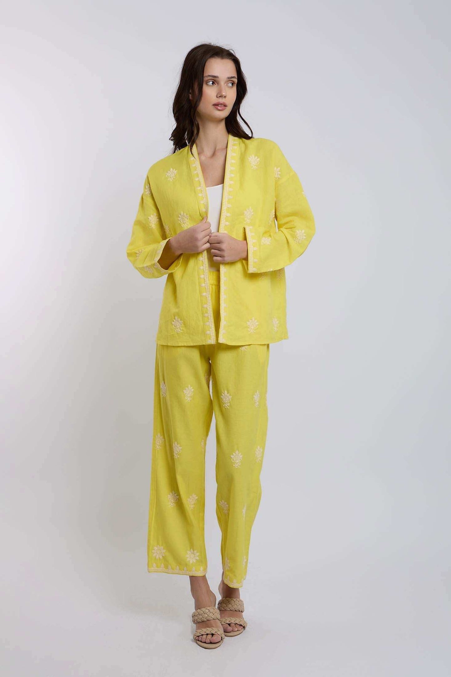 Woman wearing yellow embroidered pantsuit with white floral patterns, standing indoors