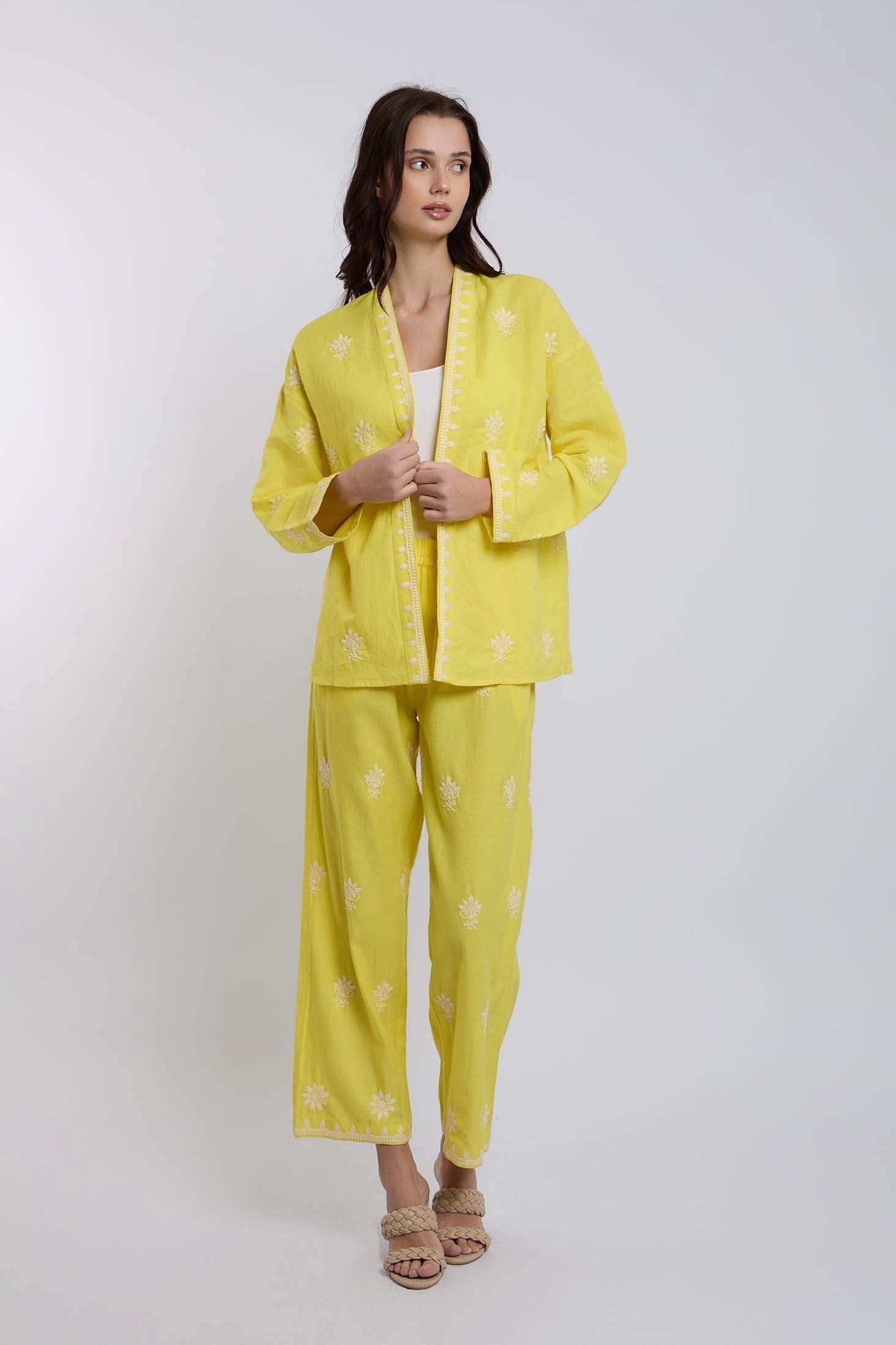 Woman wearing yellow embroidered pantsuit with white floral patterns, standing indoors