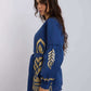 Woman in blue long-sleeve blouse with gold geometric patterns and waist belt, side view