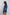 Woman in blue long-sleeve blouse with gold geometric patterns and waist belt, side view