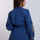 Woman wearing a blue long-sleeve blouse with gold embroidery and beige pants, back view