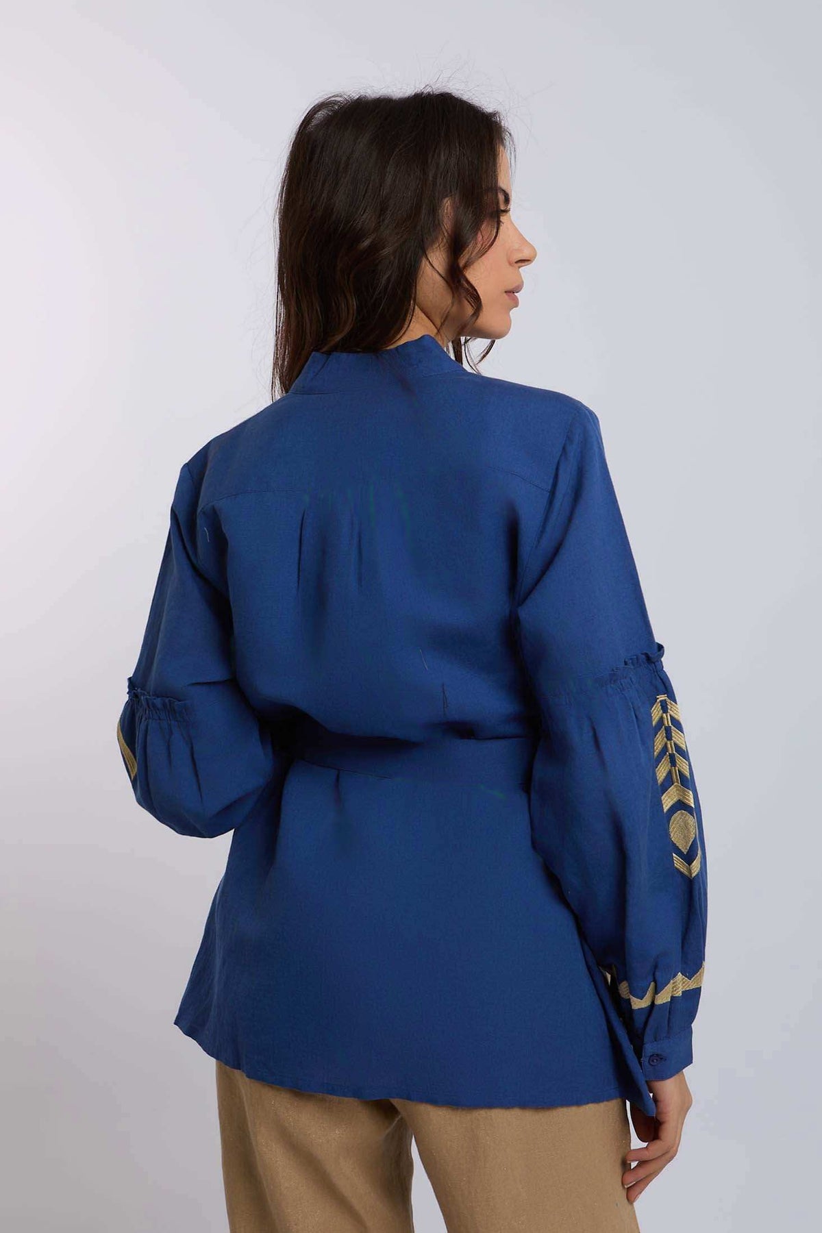 Woman wearing a blue long-sleeve blouse with gold embroidery and beige pants, back view