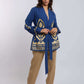 Woman wearing a blue and gold patterned long-sleeve blouse with a waist tie and beige pants