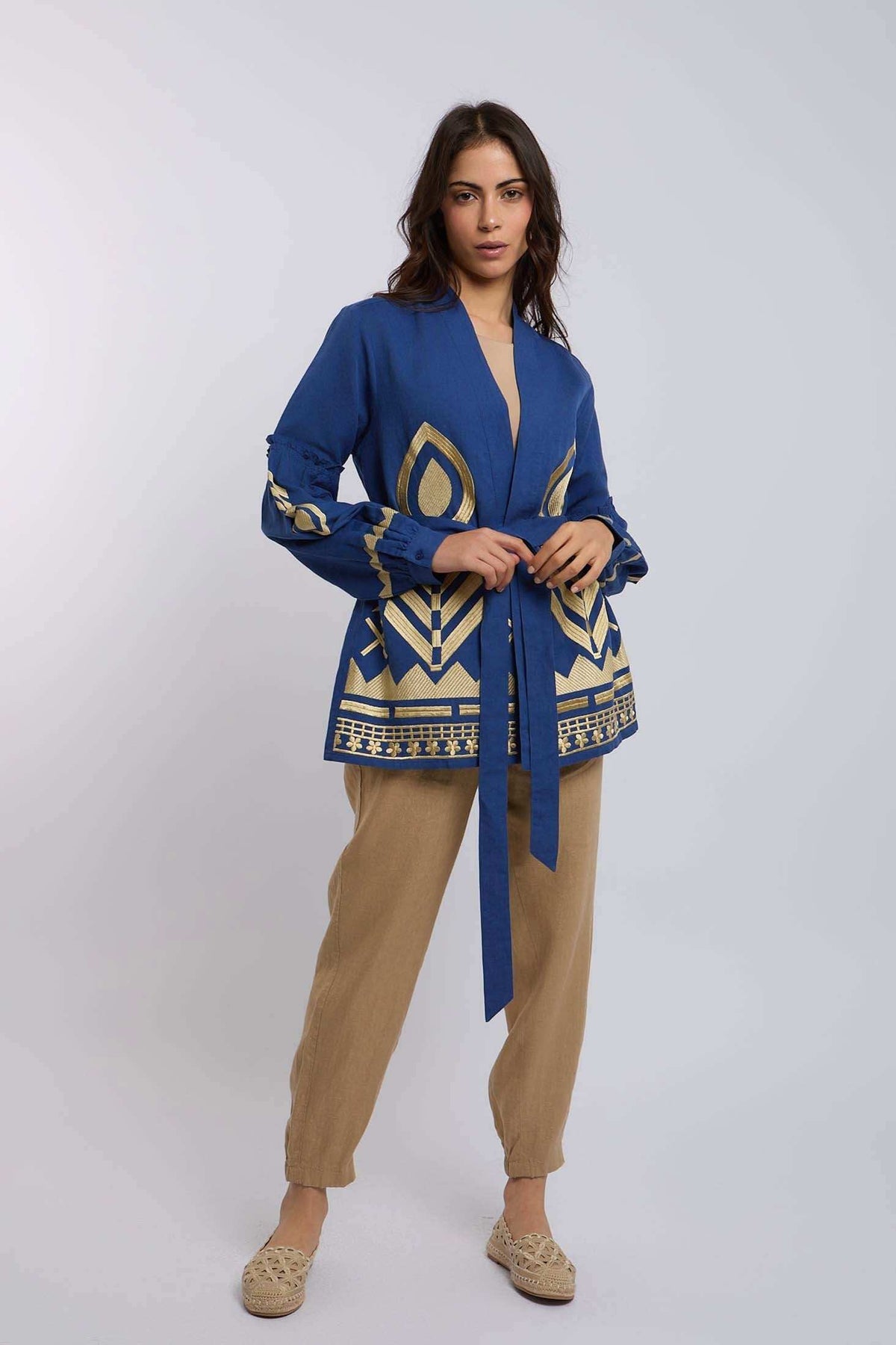 Woman wearing a blue and gold patterned long-sleeve blouse with a waist tie and beige pants