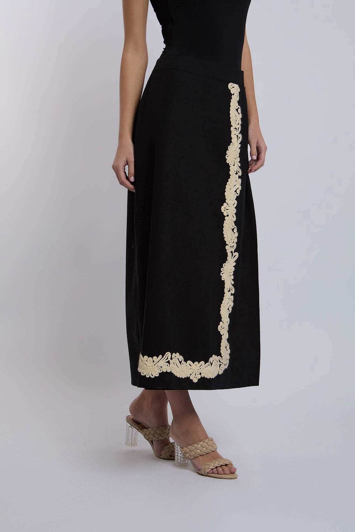 Black midi skirt with beige floral embroidery, worn by woman in heeled sandals