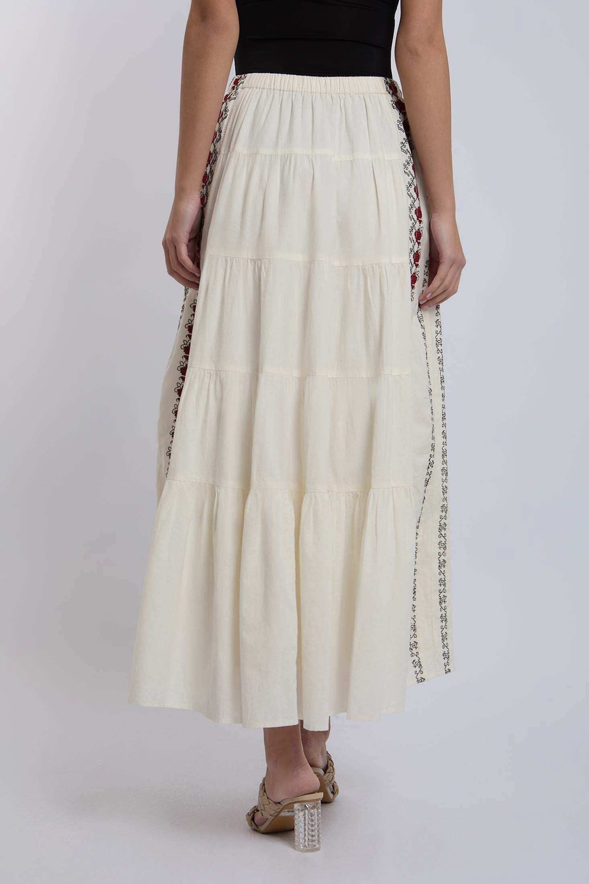 Woman wearing a tiered cream maxi skirt with side embroidery, back view.