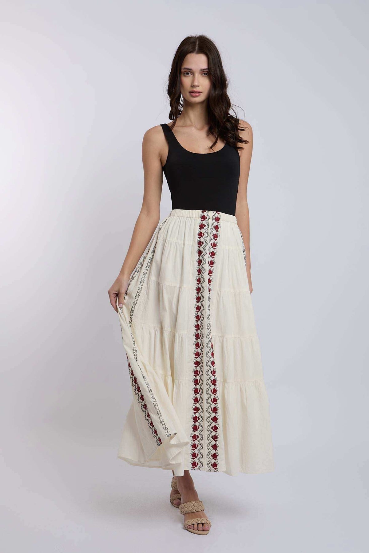 Woman wearing a sleeveless black top and long cream maxi skirt with red embroidered patterns