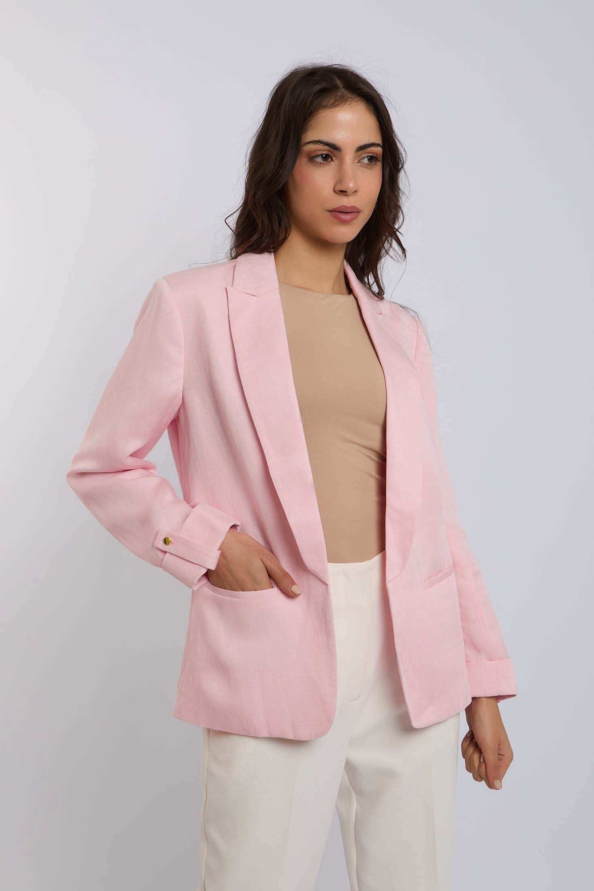 Woman wearing a light pink blazer, beige top, and white trousers in studio setting