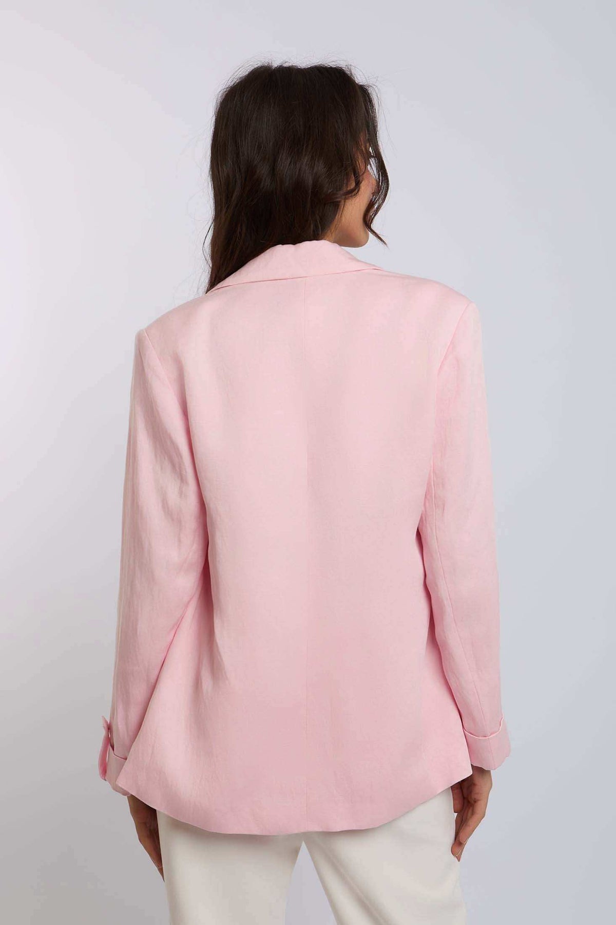 Woman wearing a light pink blazer and white pants, back view, casual fashion style