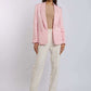 Woman wearing a light pink blazer, beige top, and cream trousers in a studio.