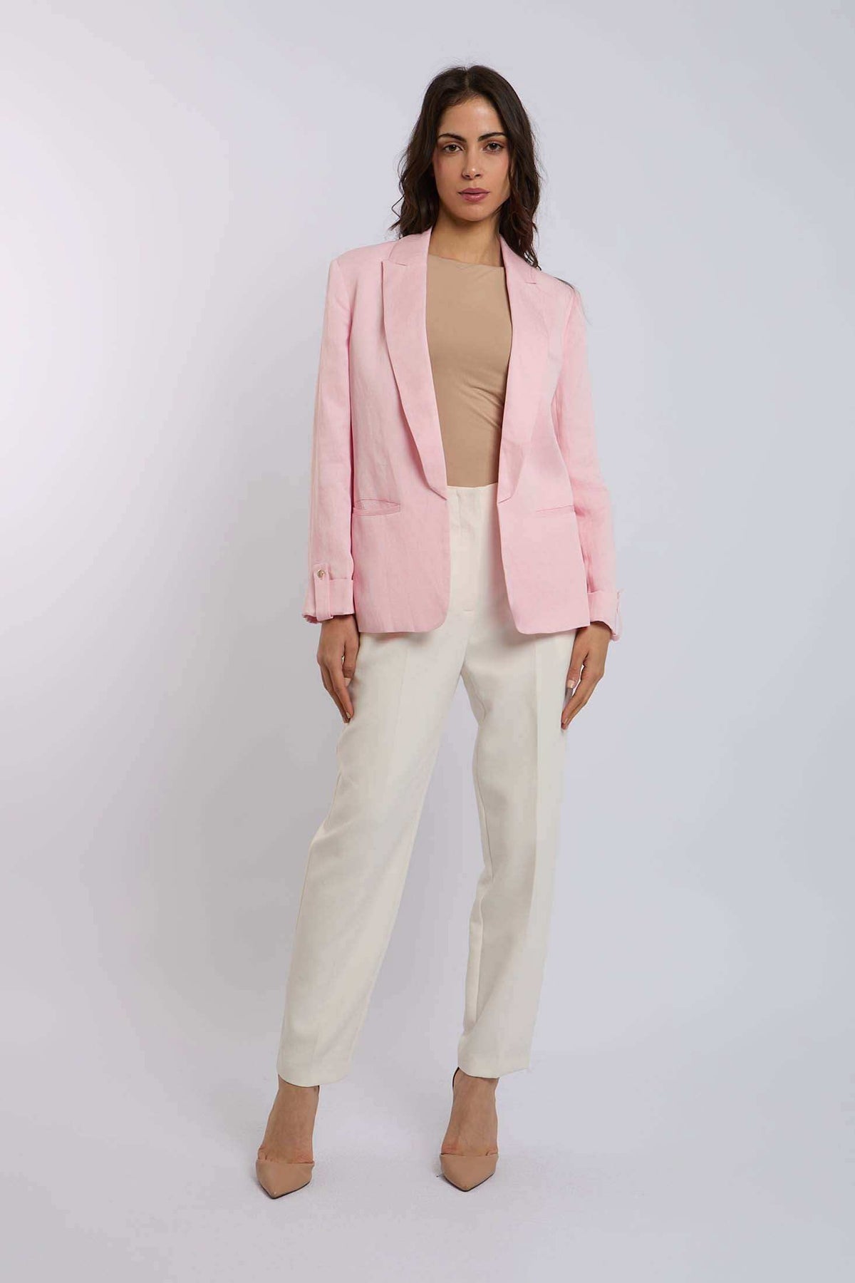 Woman wearing a light pink blazer, beige top, and cream trousers in a studio.