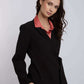 Woman in black blazer with salmon pink blouse, posing against plain background