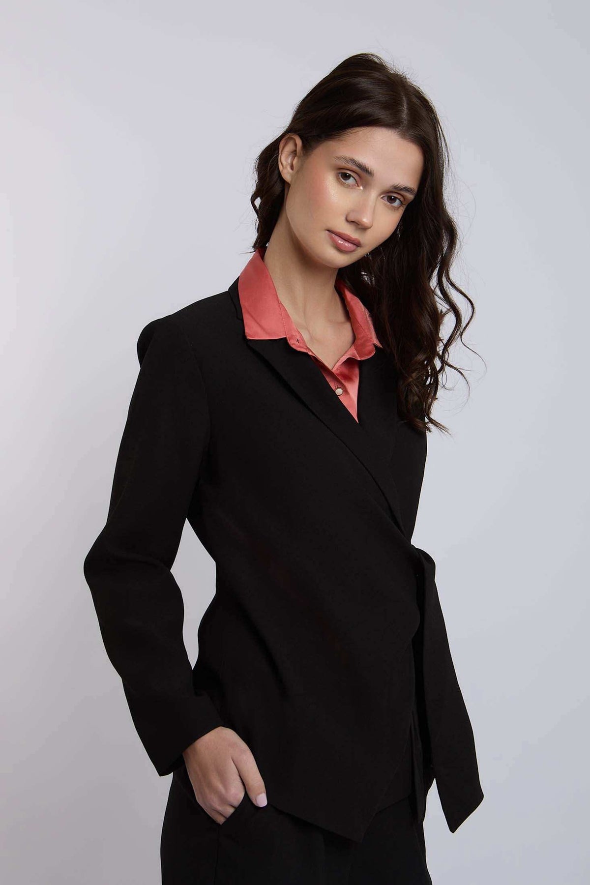 Woman in black blazer with salmon pink blouse, posing against plain background