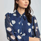 Woman wearing a Dalydress blue polka dot blouse with tie-neck and semi-sheer sleeves