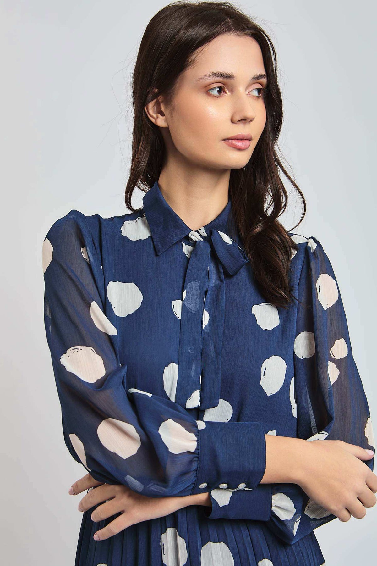 Woman wearing a Dalydress blue polka dot blouse with tie-neck and semi-sheer sleeves