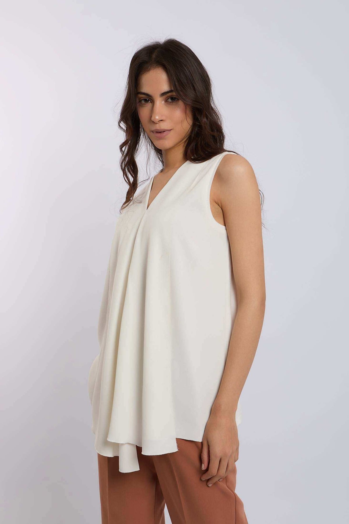 Woman wearing a sleeveless white flowy blouse with V-neck and peach trousers
