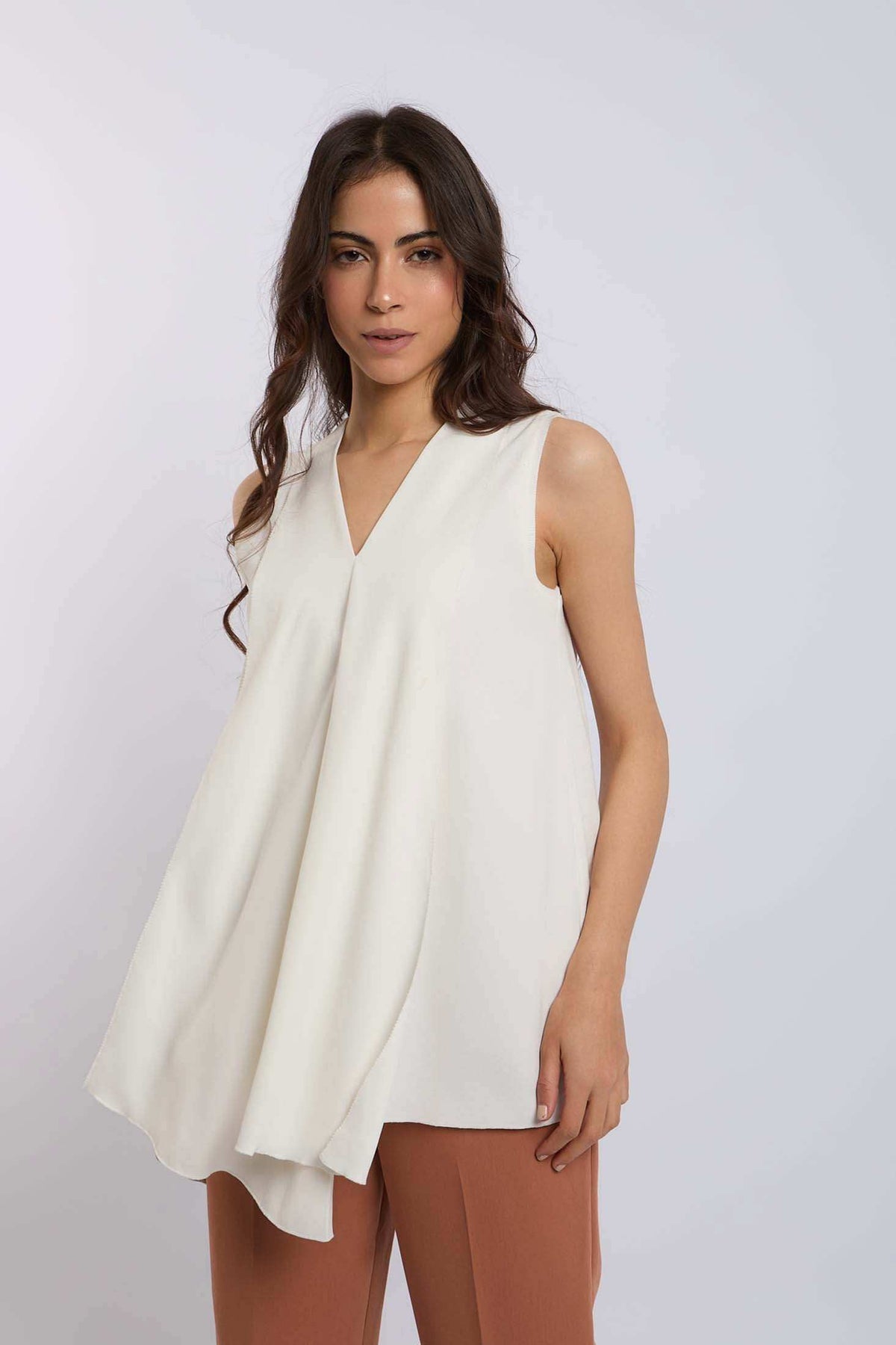 Woman modeling sleeveless white V-neck top with flowy design, paired with brown pants