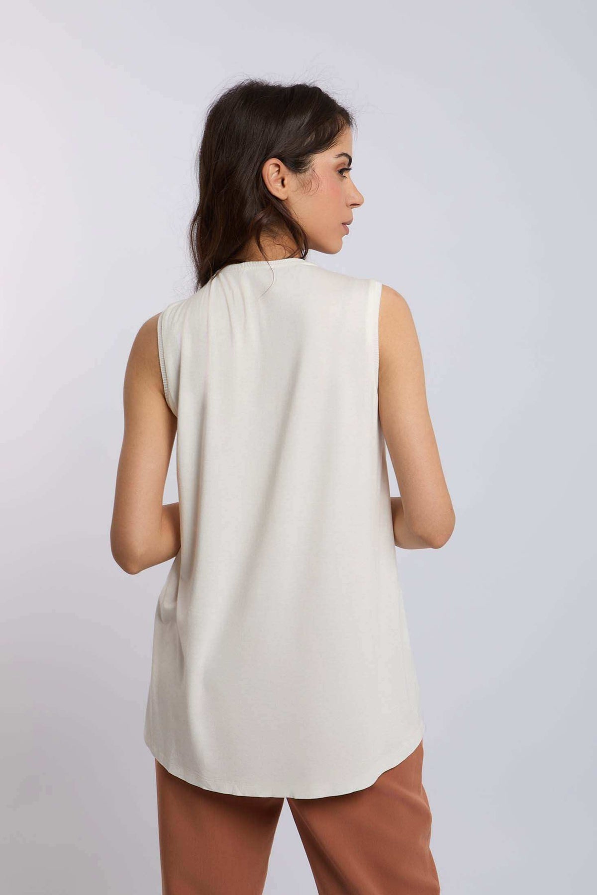 Woman wearing sleeveless ivory top with brown pants, photographed from the back