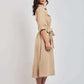 Woman in beige midi shirt dress with tie waist and rolled sleeves, casual sneakers, studio background