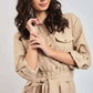 Woman modeling beige long-sleeve belted shirt dress with chest pockets and rolled cuffs.