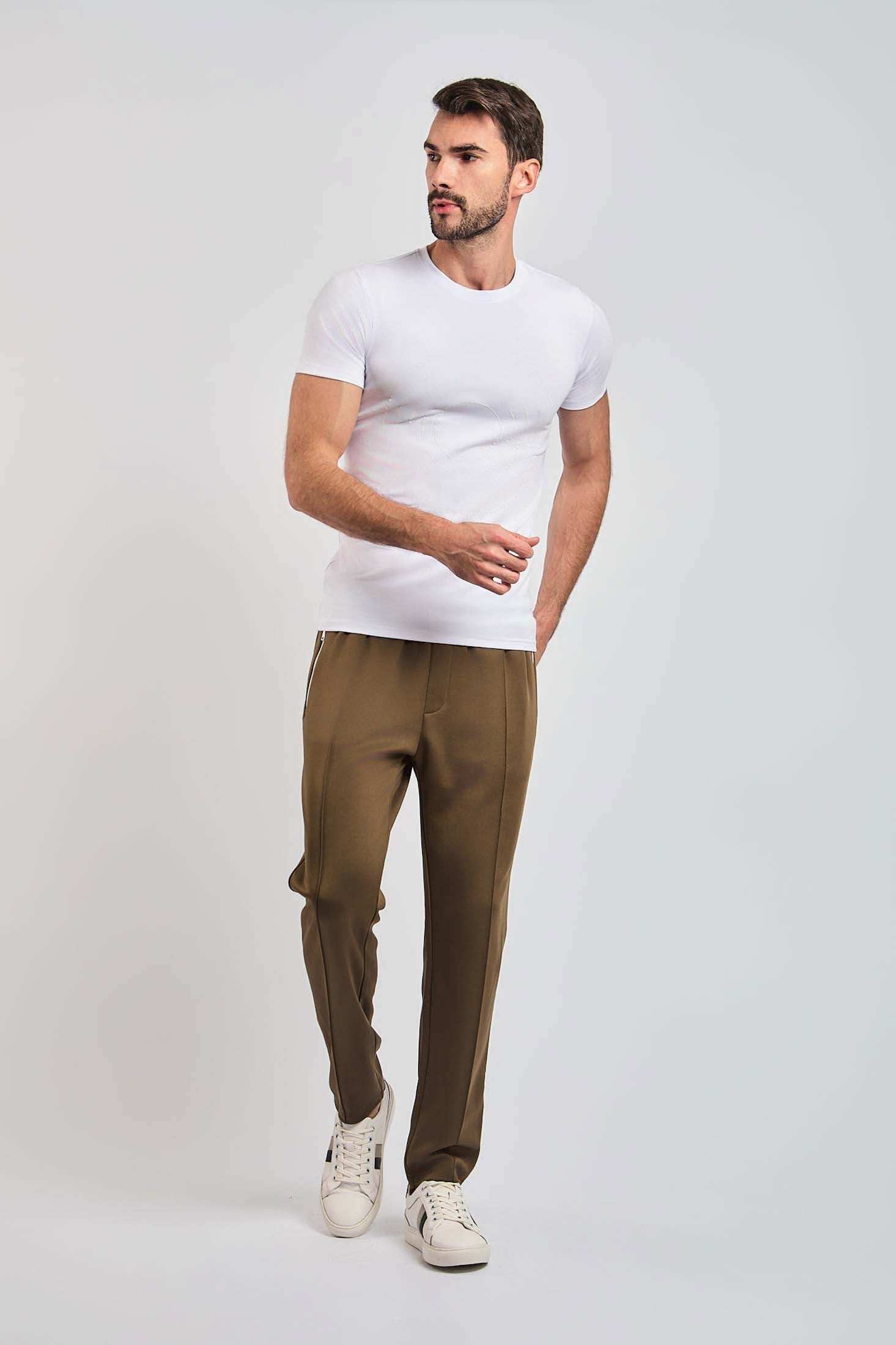 Man in white short sleeve t-shirt, brown casual pants, and white sneakers on plain background
