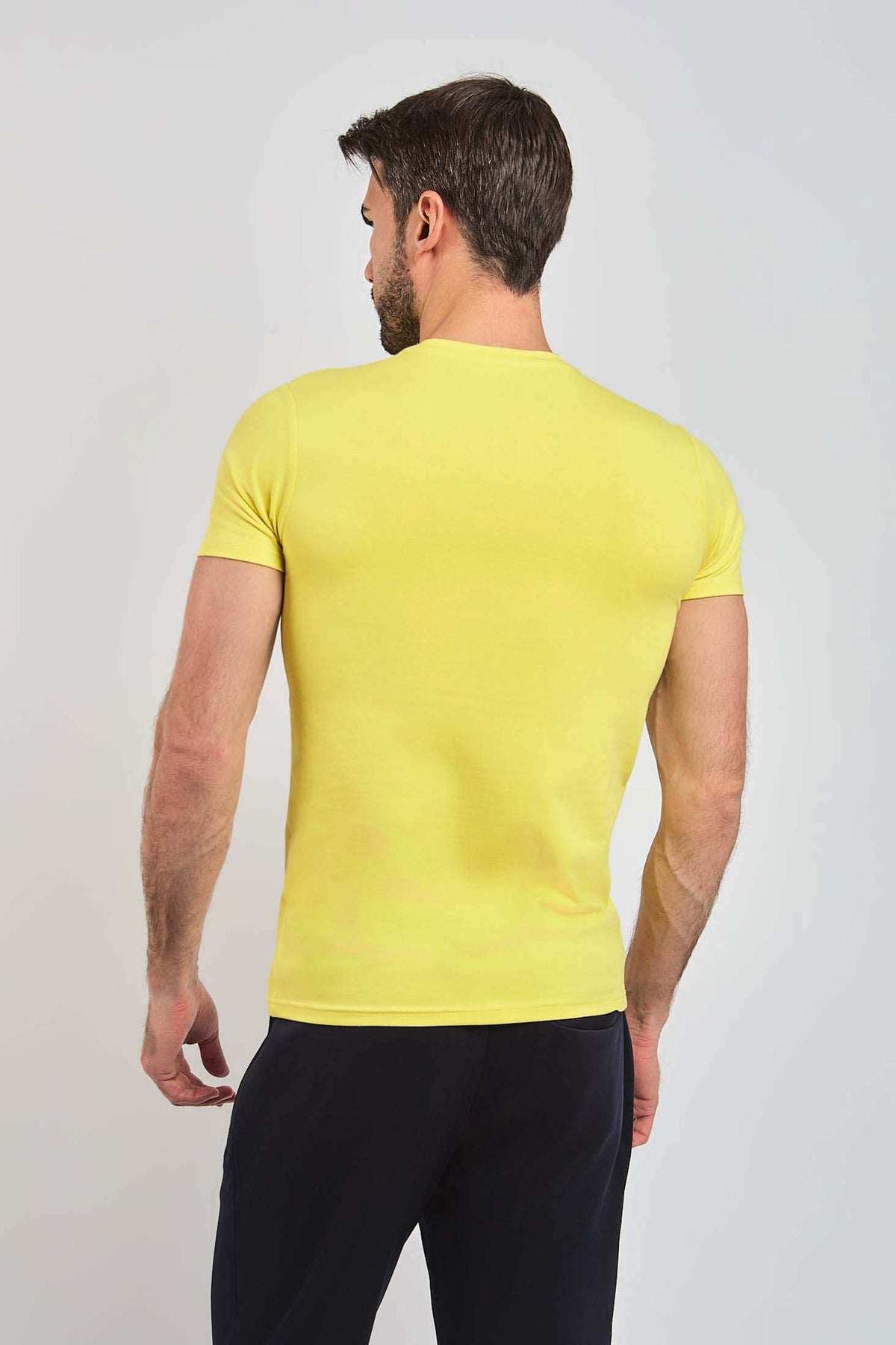 Man wearing a plain yellow short-sleeve t-shirt, back view, with black pants