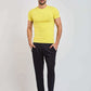 Man in a yellow t-shirt, black pants, and white sneakers posing on a plain background