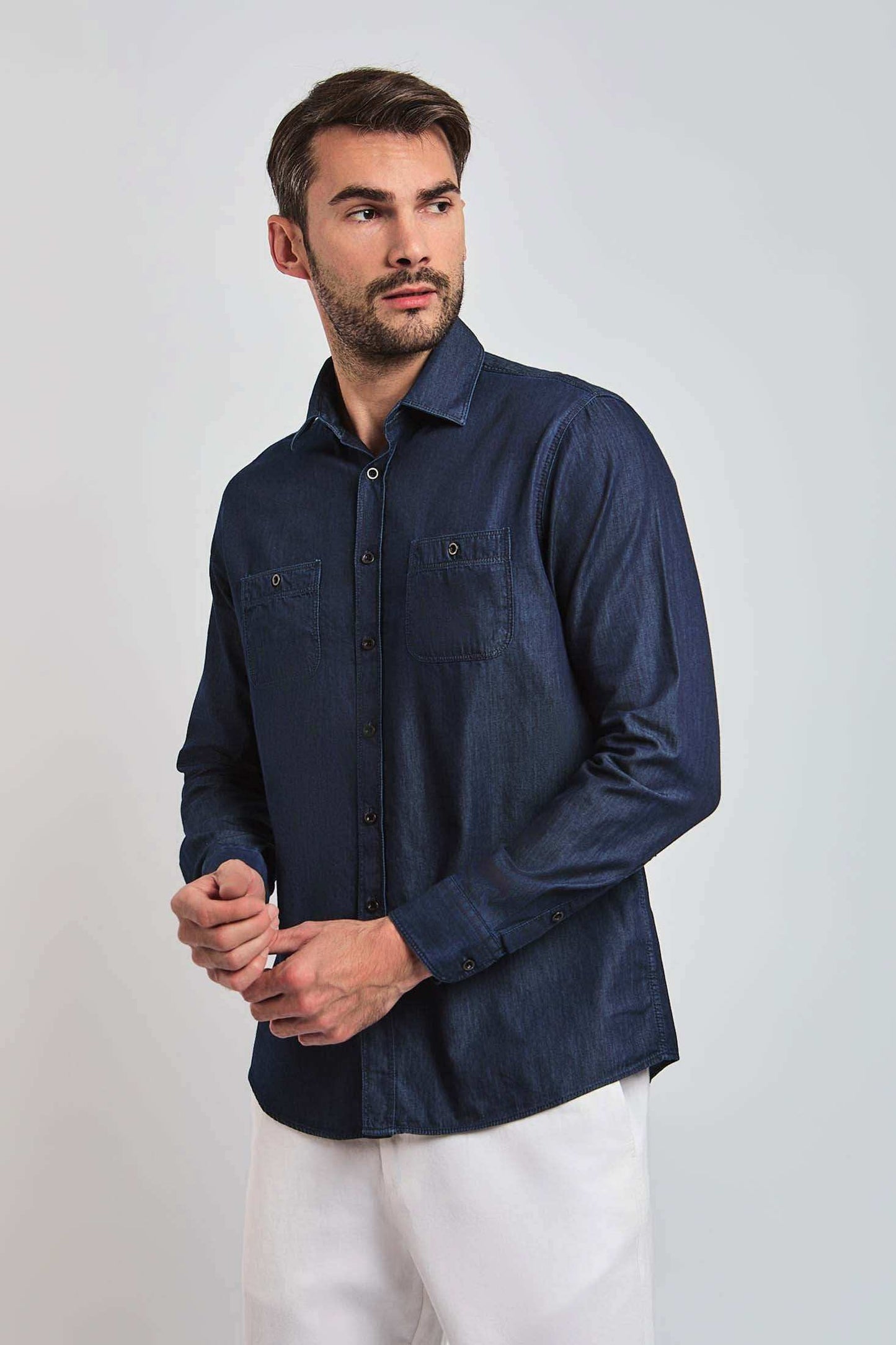 Man wearing a long sleeve dark denim shirt with chest pockets and white pants