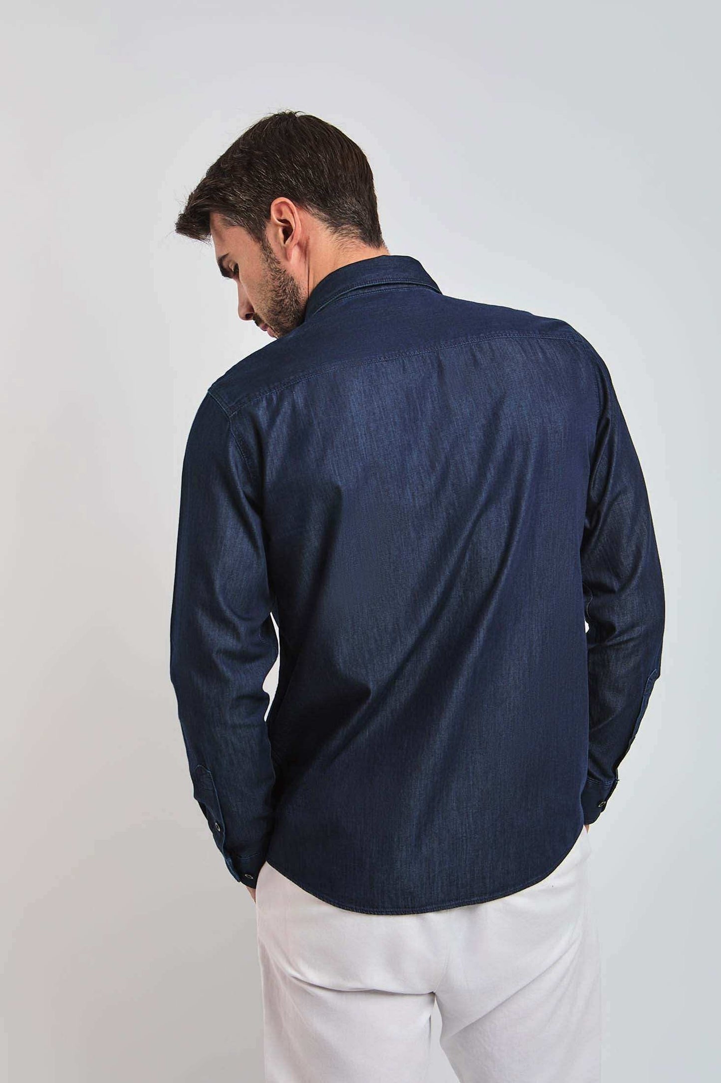Man wearing long sleeve dark denim shirt and white pants, back view, casual style