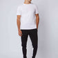 Man wearing white t-shirt with embossed text, black joggers with white stripes, and sneakers