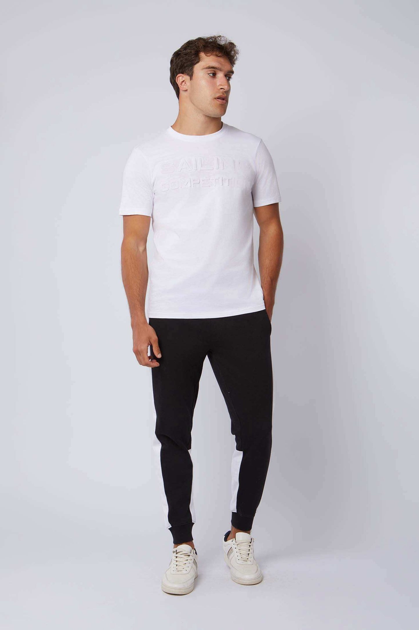 Man wearing white t-shirt with embossed text, black joggers with white stripes, and sneakers