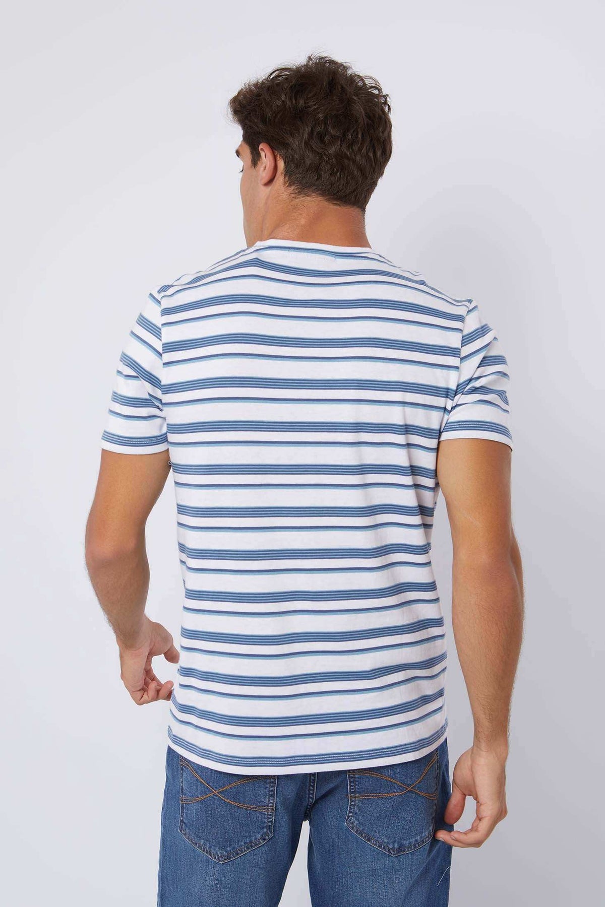 Back view of man wearing a white and blue striped short-sleeve t-shirt with jeans