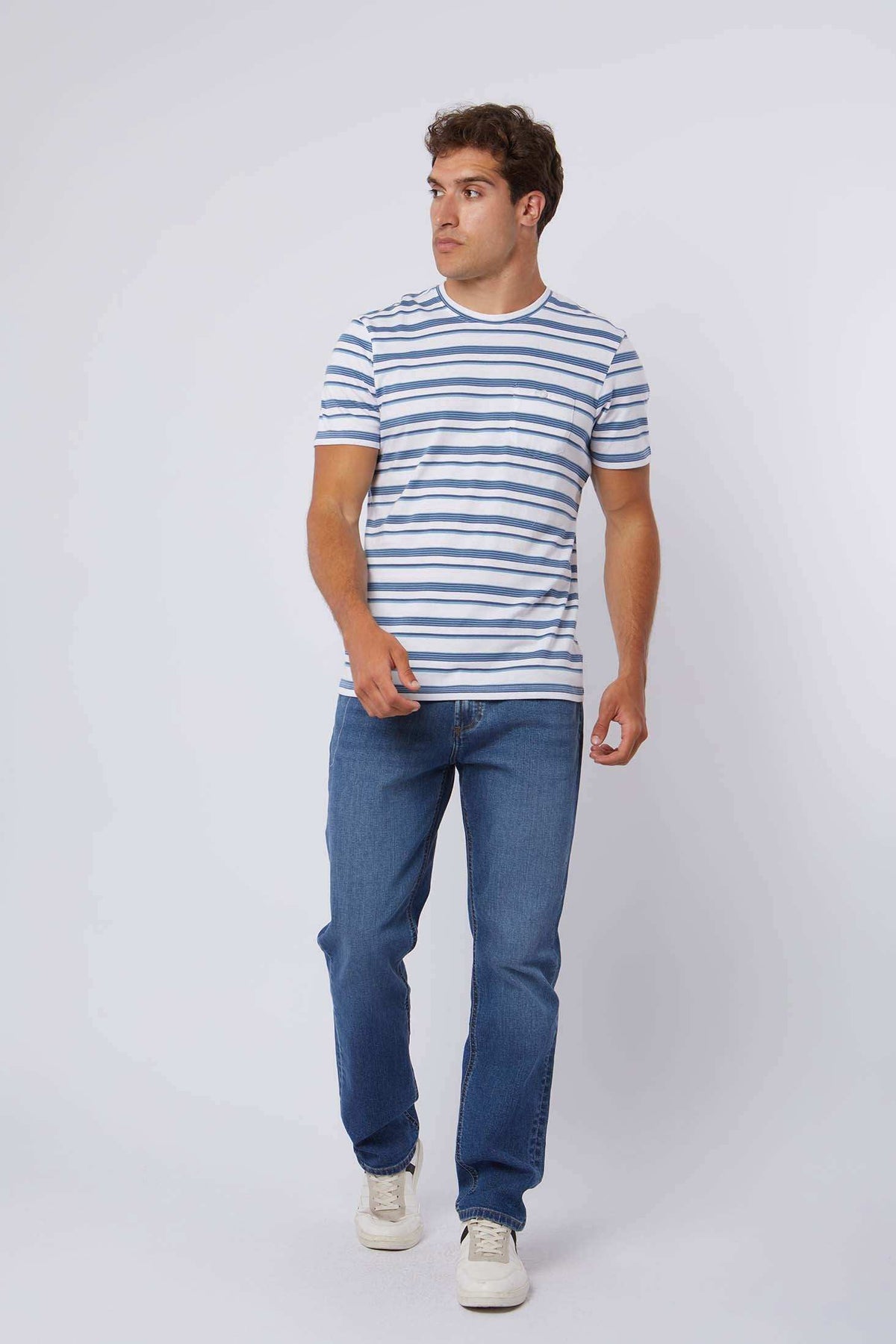 Man wearing blue and white striped t-shirt, blue jeans, and white sneakers