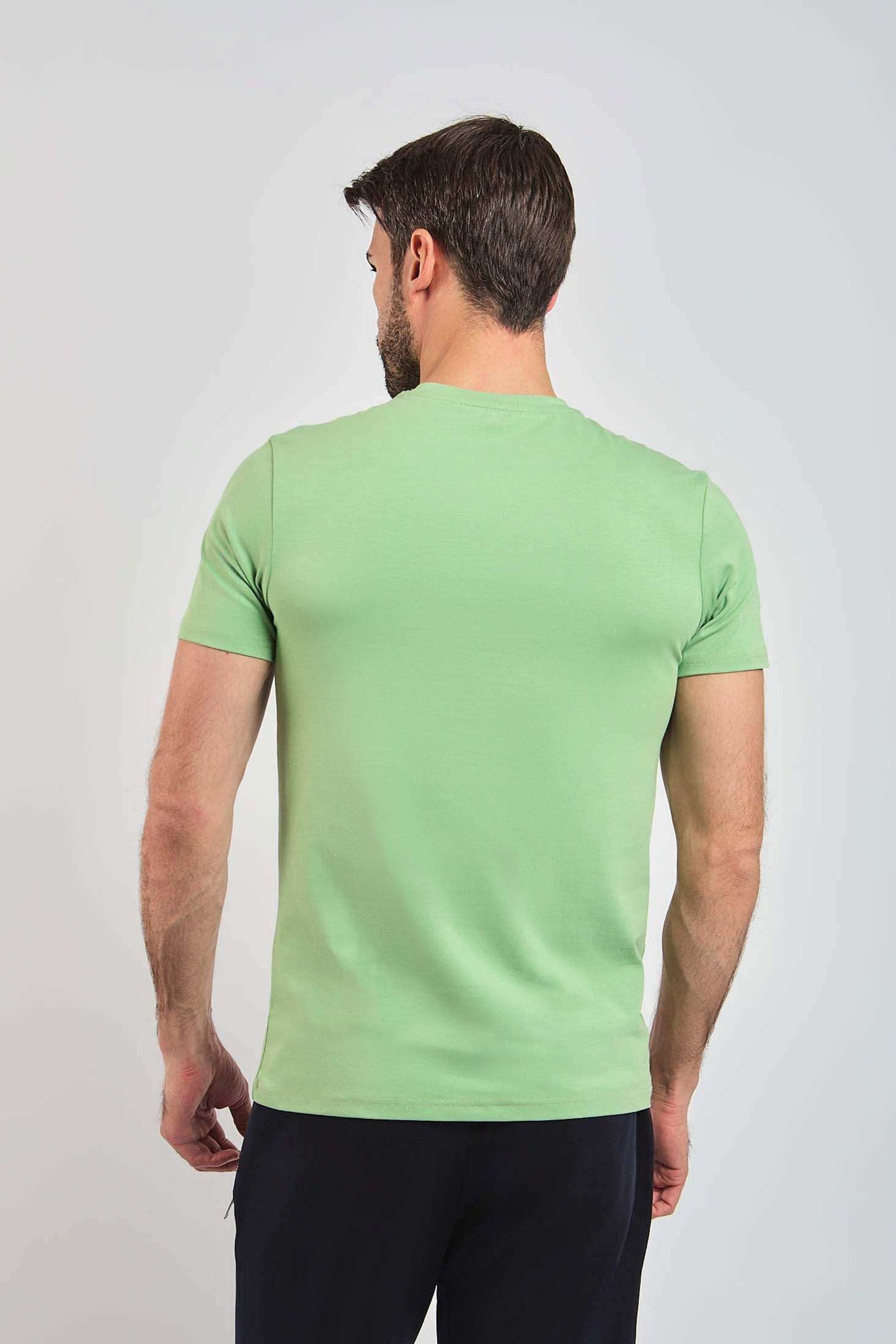 Man wearing light green short sleeve t-shirt, viewed from the back, on plain background