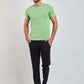 Man wearing light green t-shirt, black pants, and white sneakers on plain background